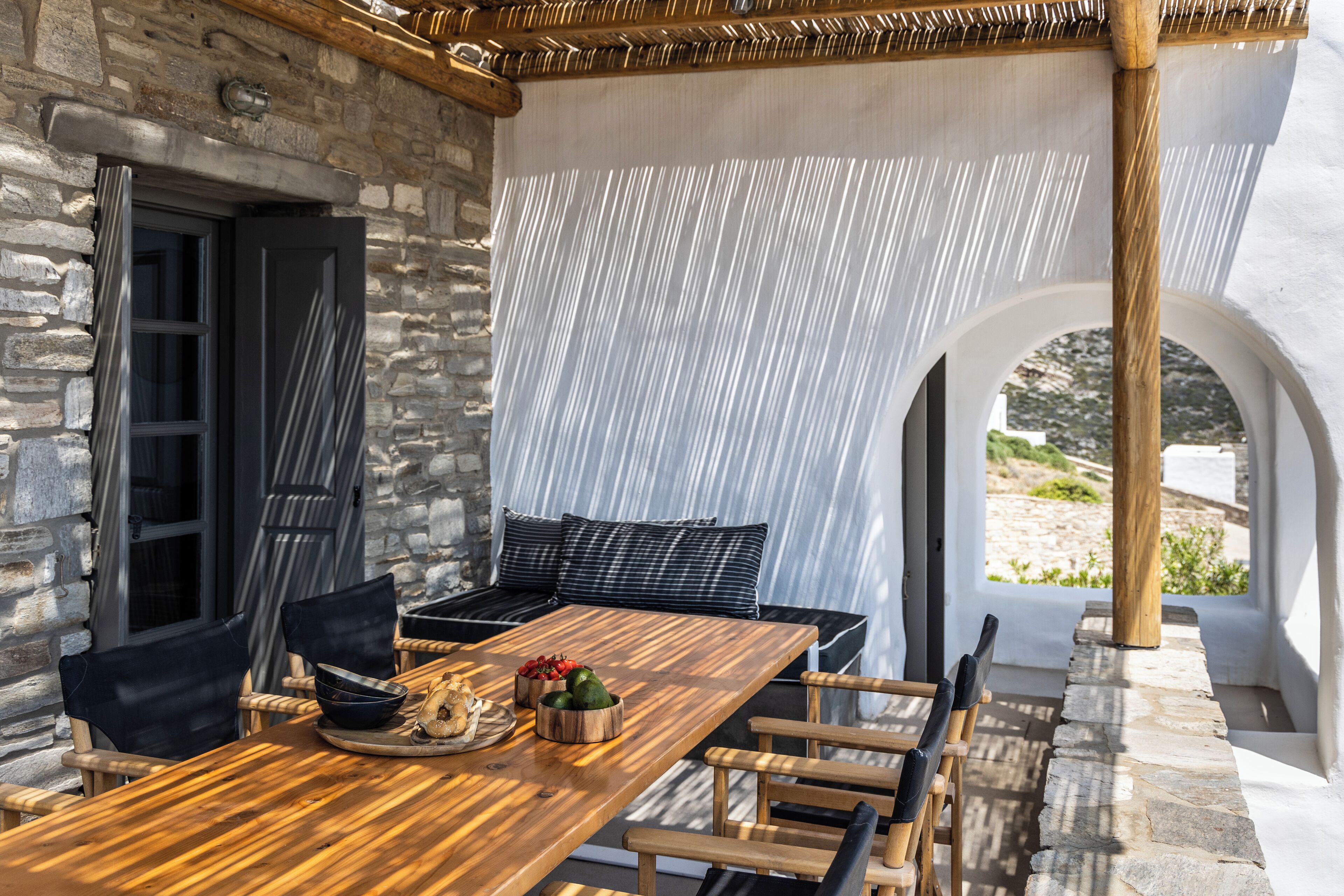A wooden dining table with chairs, a stone wall, and a view of the outdoors.
