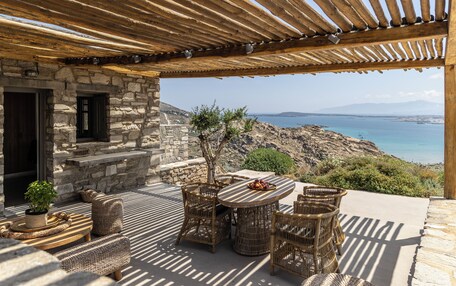A stone building with a wooden pergola, wicker furniture, and a view of the sea.