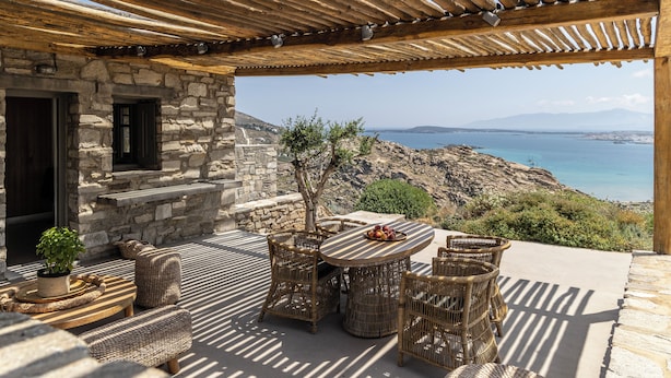 A stone building with a wooden pergola, wicker furniture, and a view of the sea.