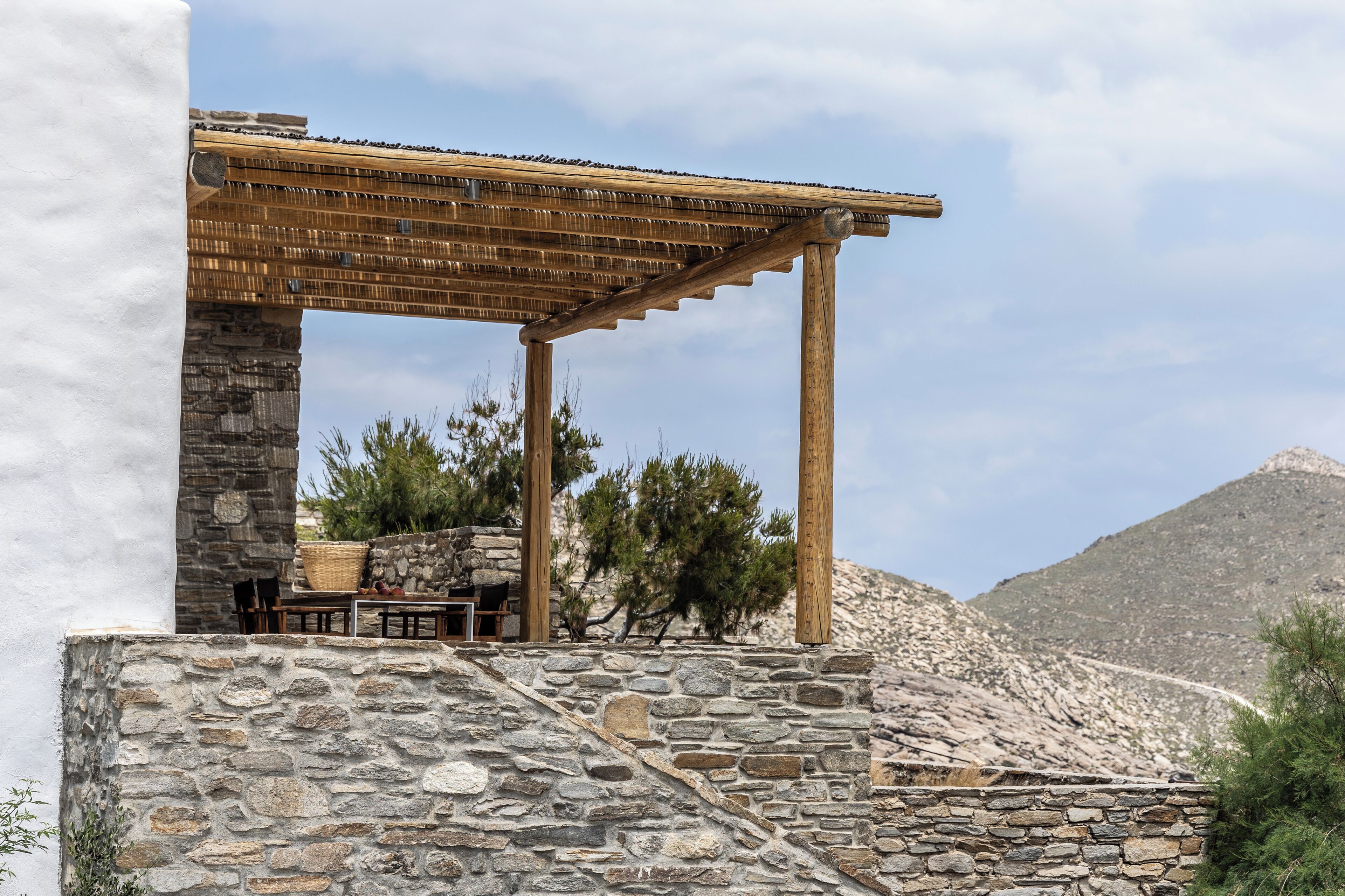 A stone structure with a wooden pergola, outdoor seating, and a mountainous backdrop.