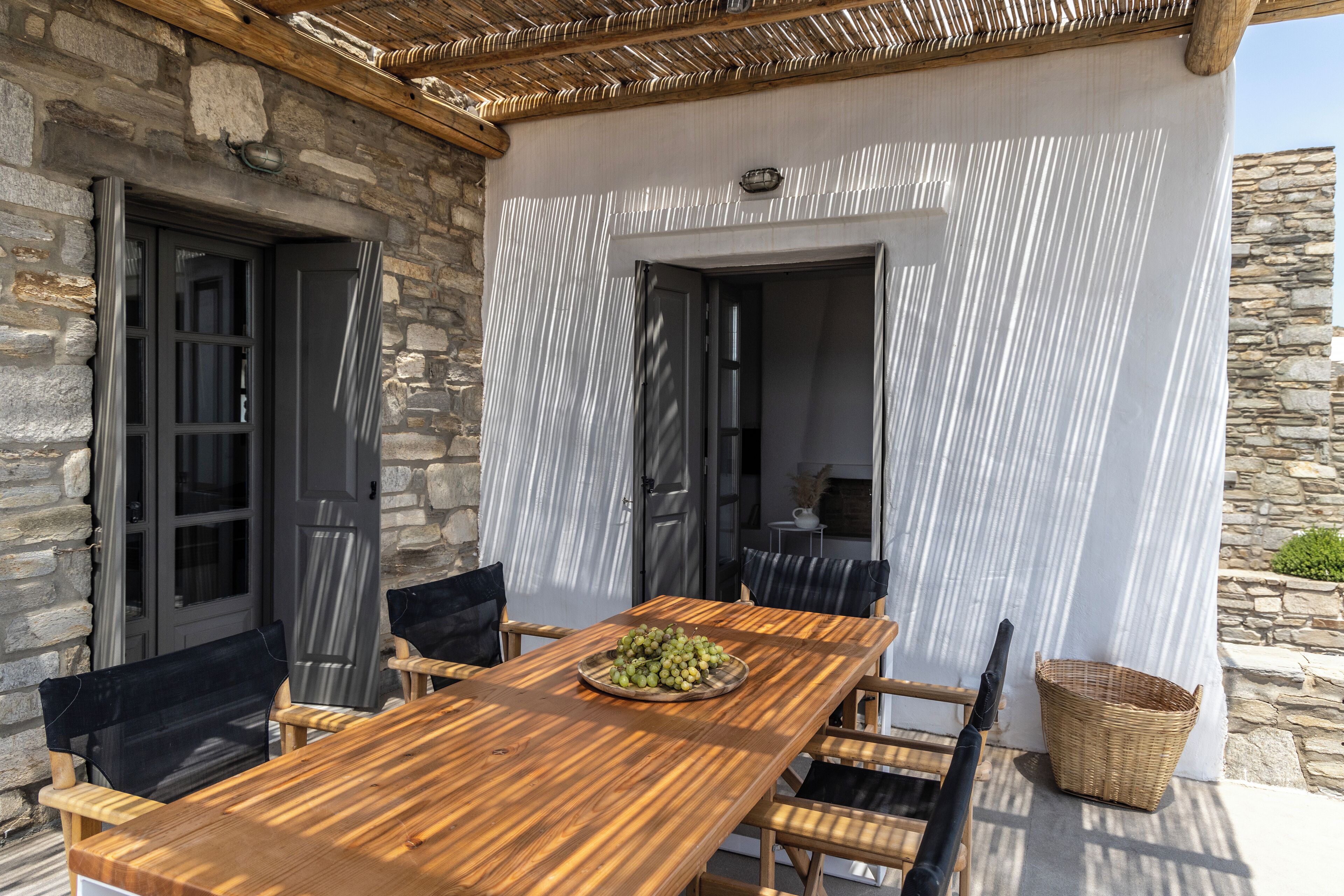 An outdoor dining area with a wooden table and chairs, a wicker basket, and a stone wall.