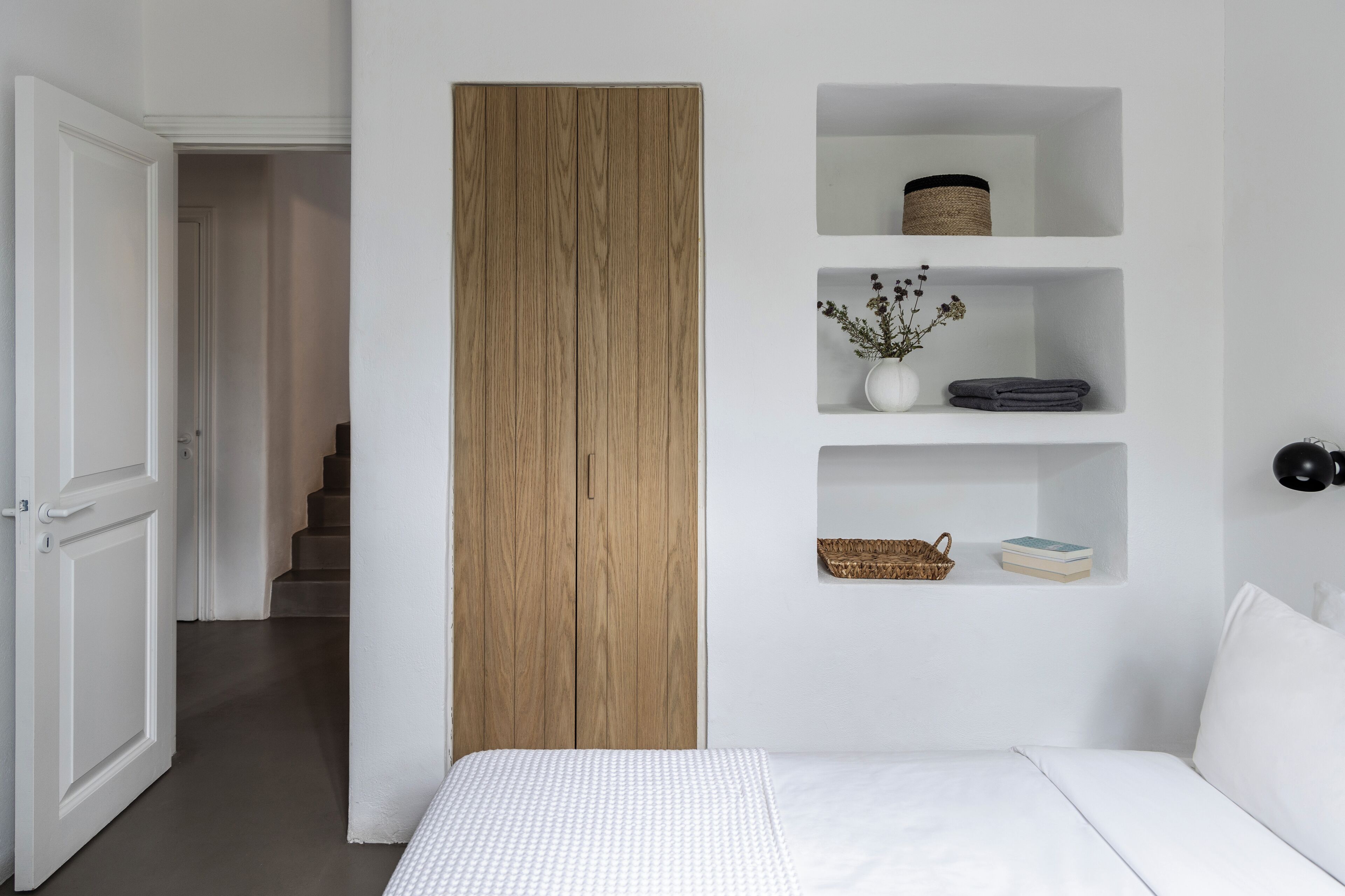 Un dormitorio con una cama, un armario de madera y tres estantes con diversos objetos.