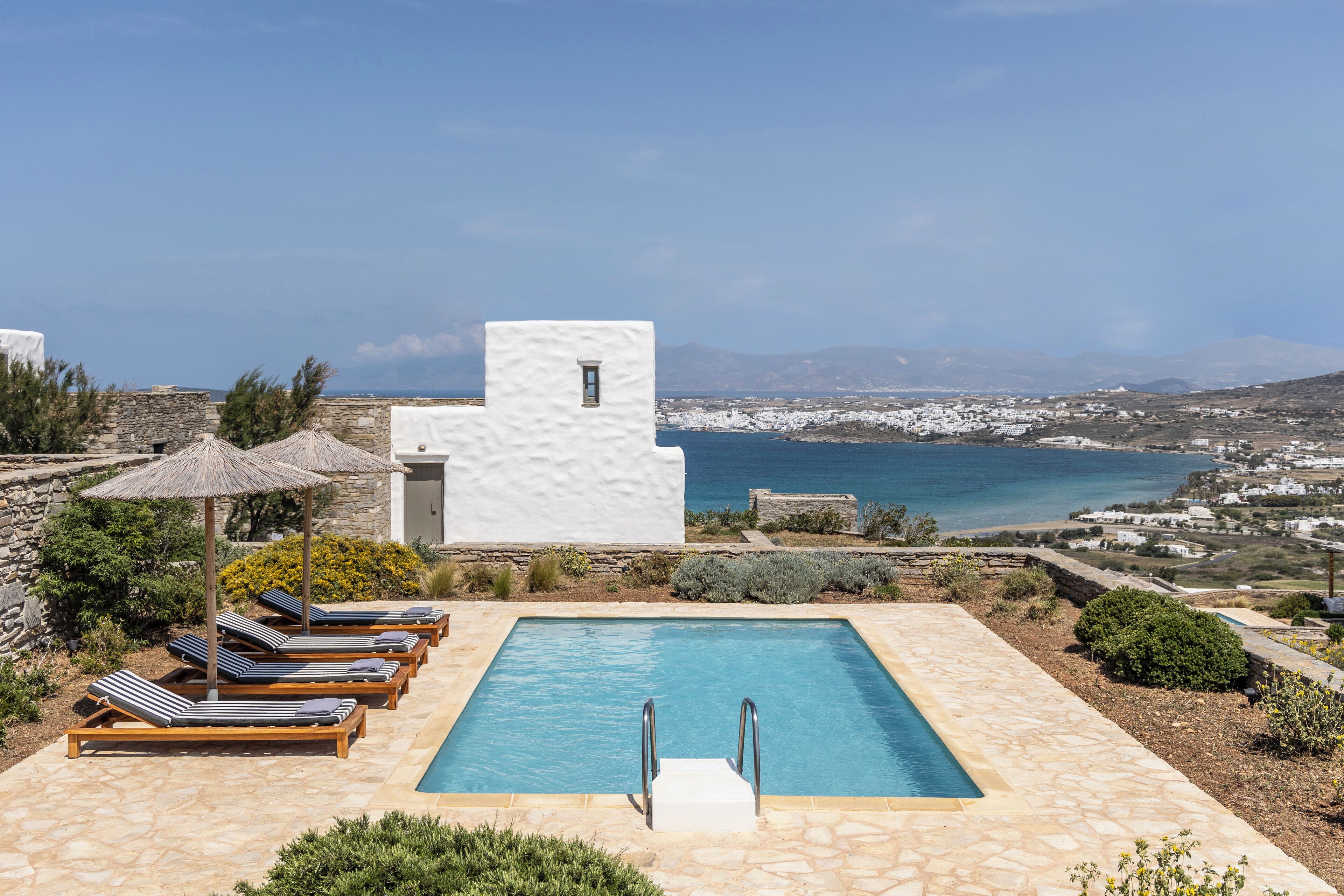 A pool area with lounge chairs and a view of the sea.