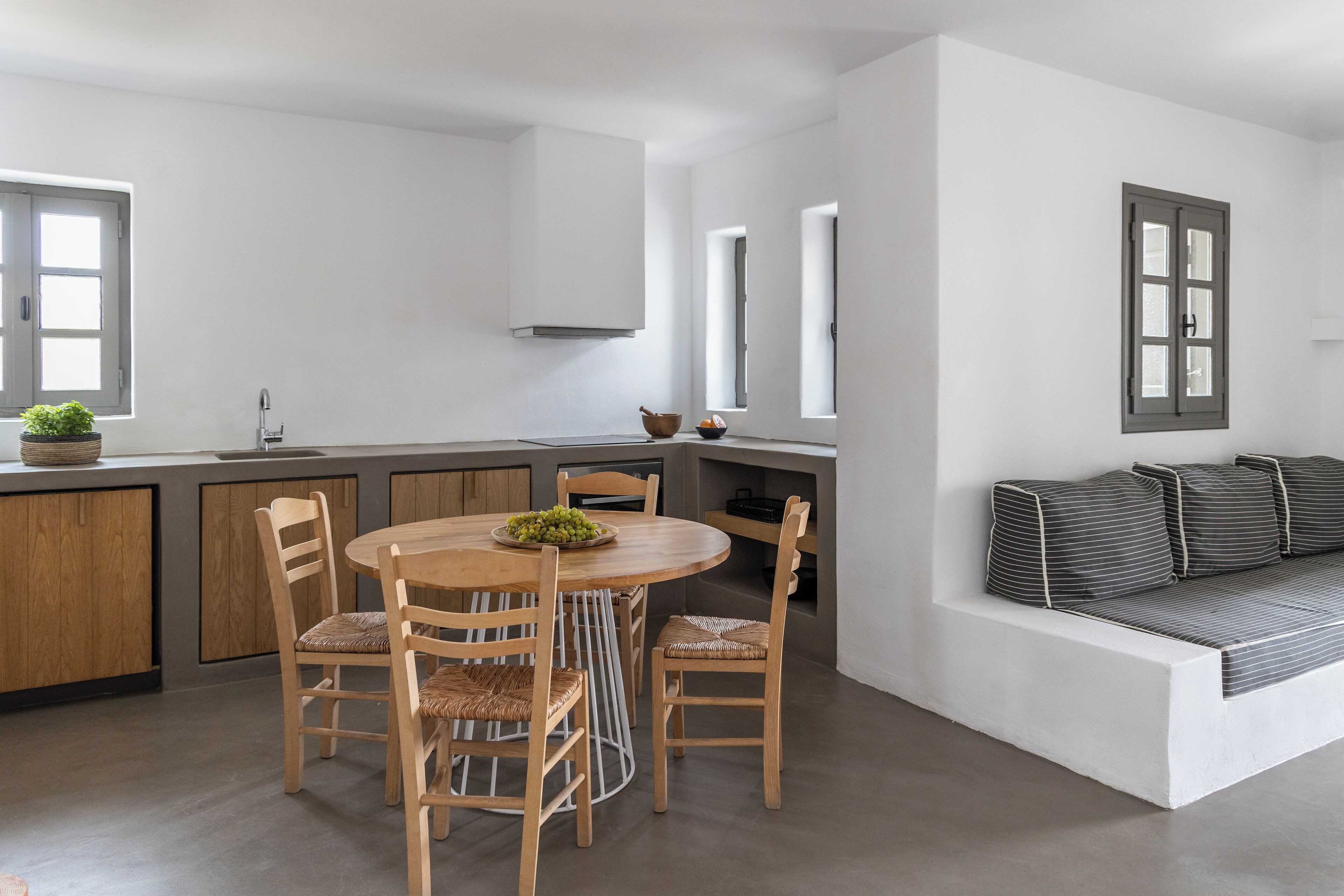 A modern kitchen with a round wooden table, four chairs, and a built-in bench with cushions.