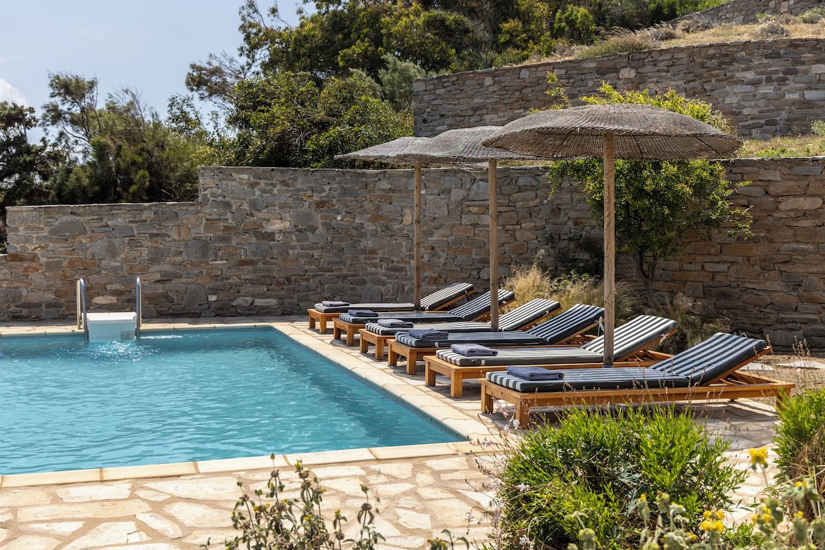 Une piscine entourée de murs de pierre et de verdure, avec des chaises longues et des parasols.