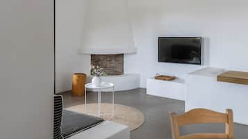 A modern living room with a fireplace, a flat-screen TV mounted on the wall, a round rug, and a wooden chair.