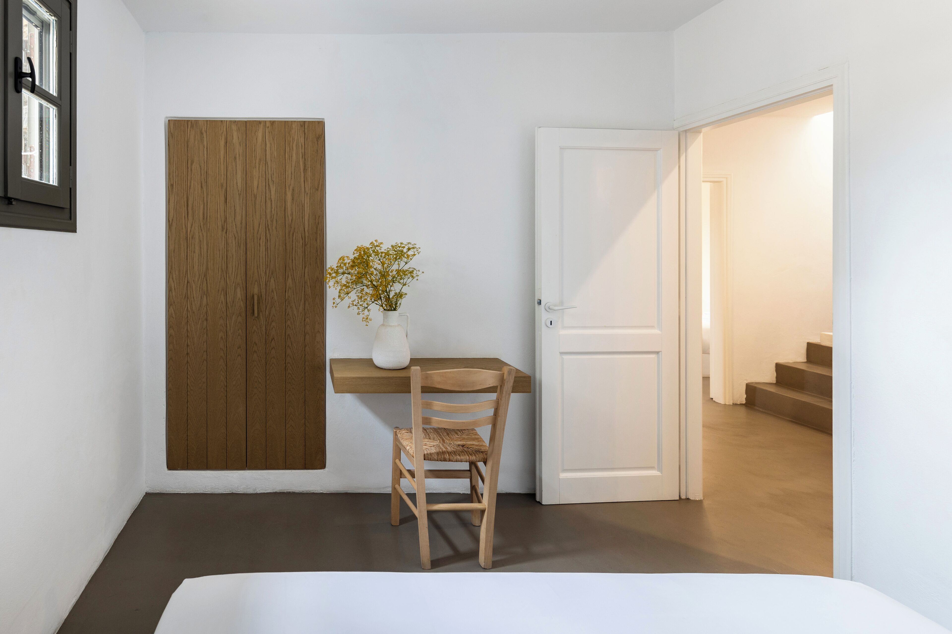 A room with a wooden panel wall, a white door, a small table with a vase of flowers, and a chair.