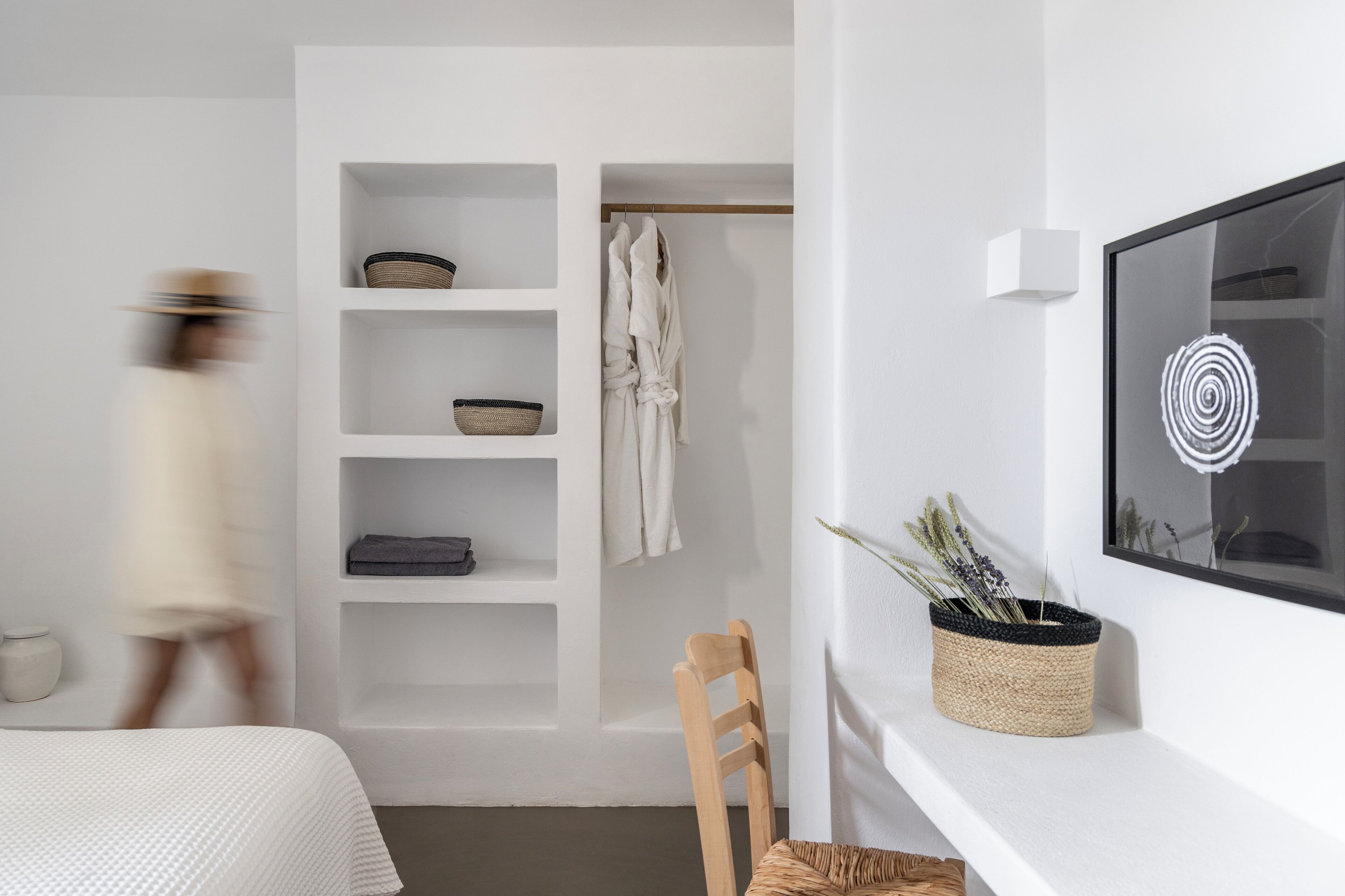 Une chambre moderne avec un lit, une chaise en bois, une armoire avec des étagères et un téléviseur fixé au mur.