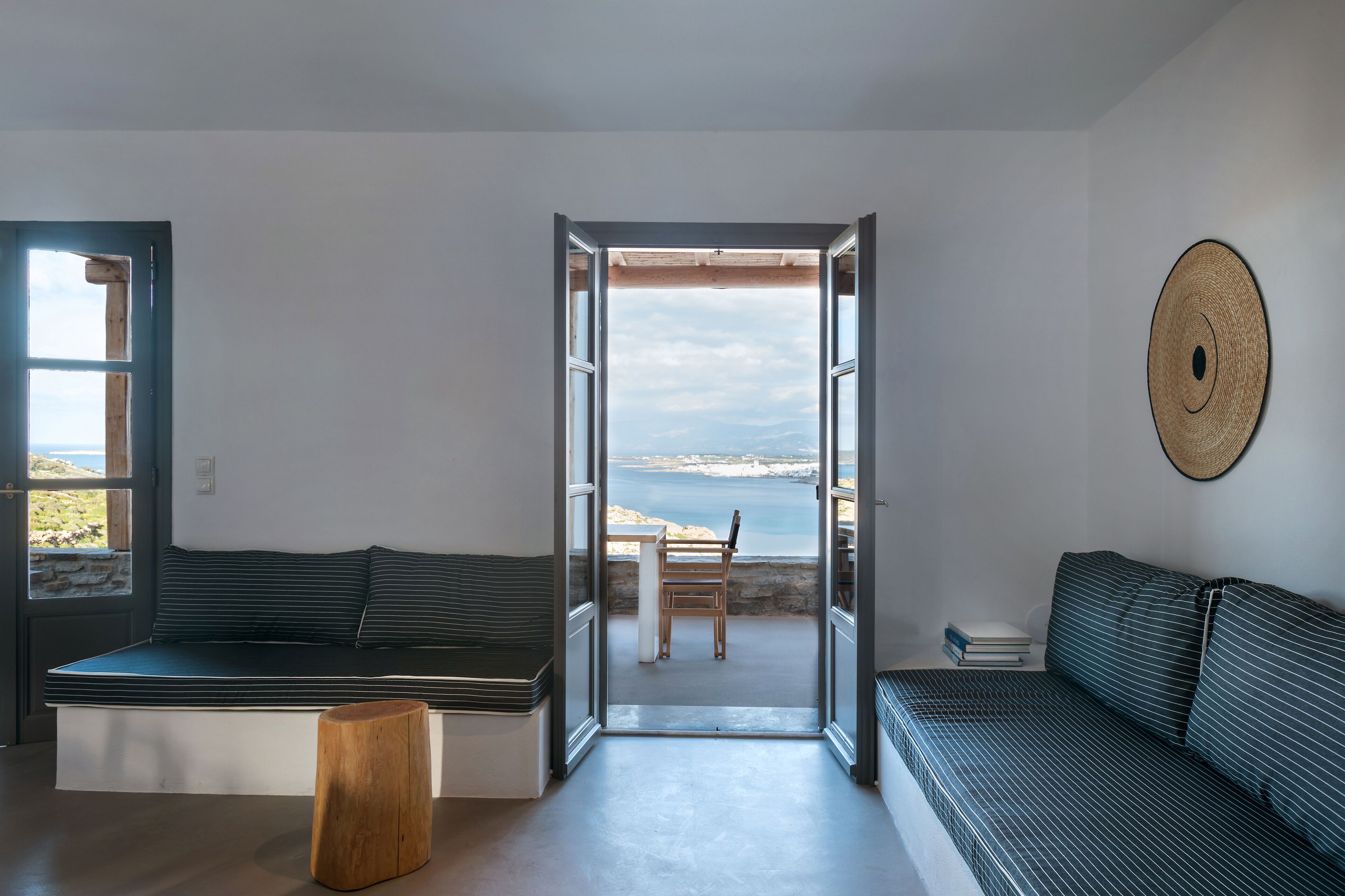 A modern living room with a sofa, a bench, and a view of the sea through open doors.