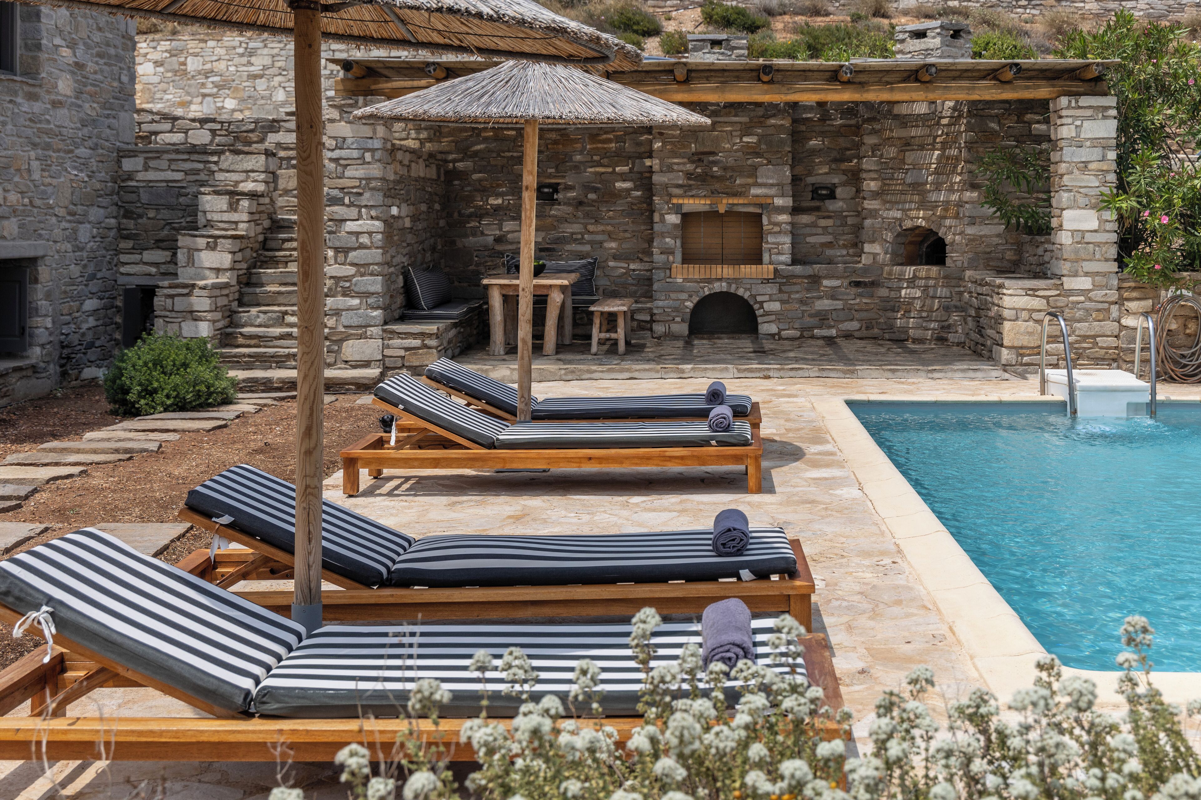 A stone building with a pool, lounge chairs, and a barbecue area.