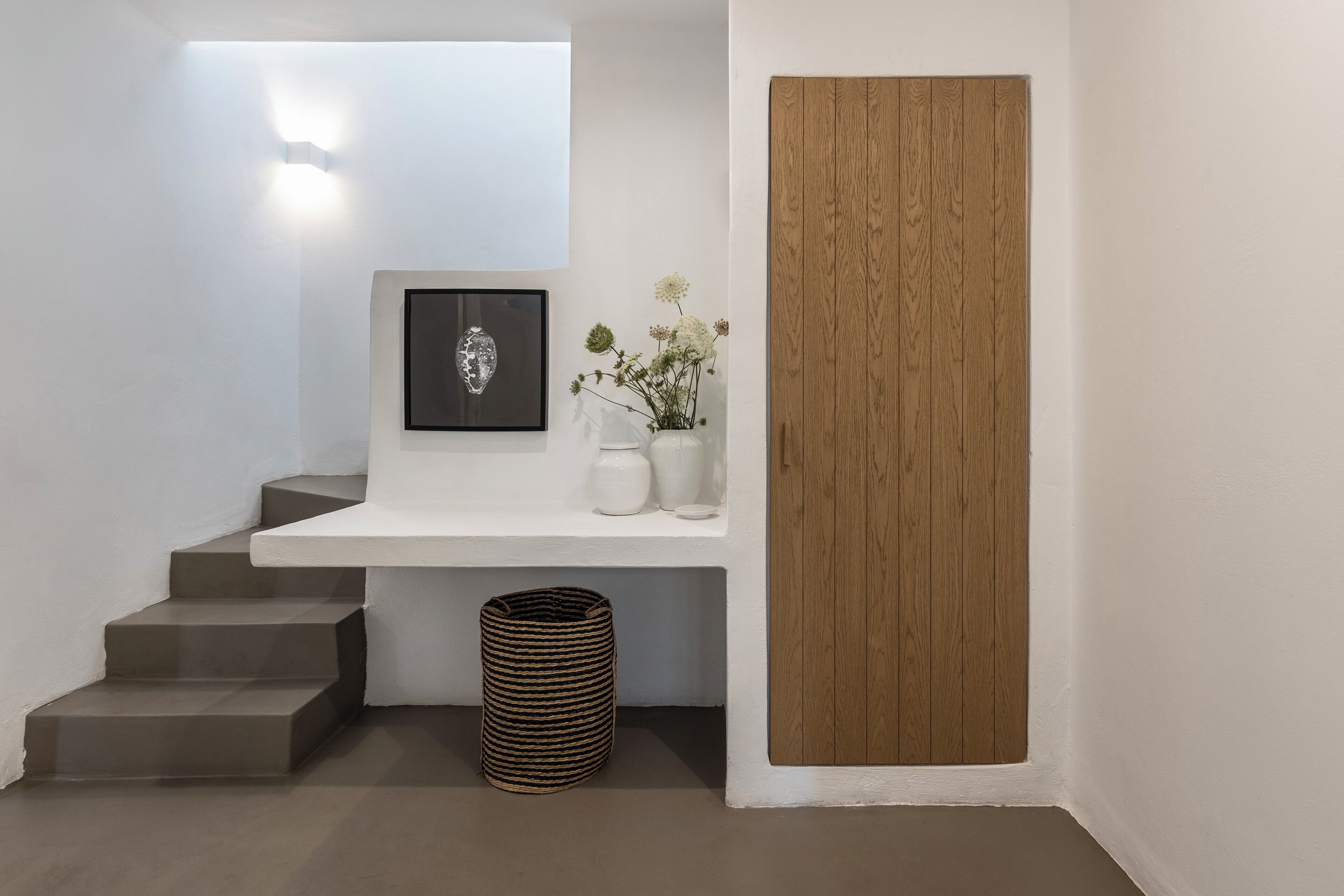 A modern interior with a staircase, a framed artwork, a vase with flowers, and a wooden door.