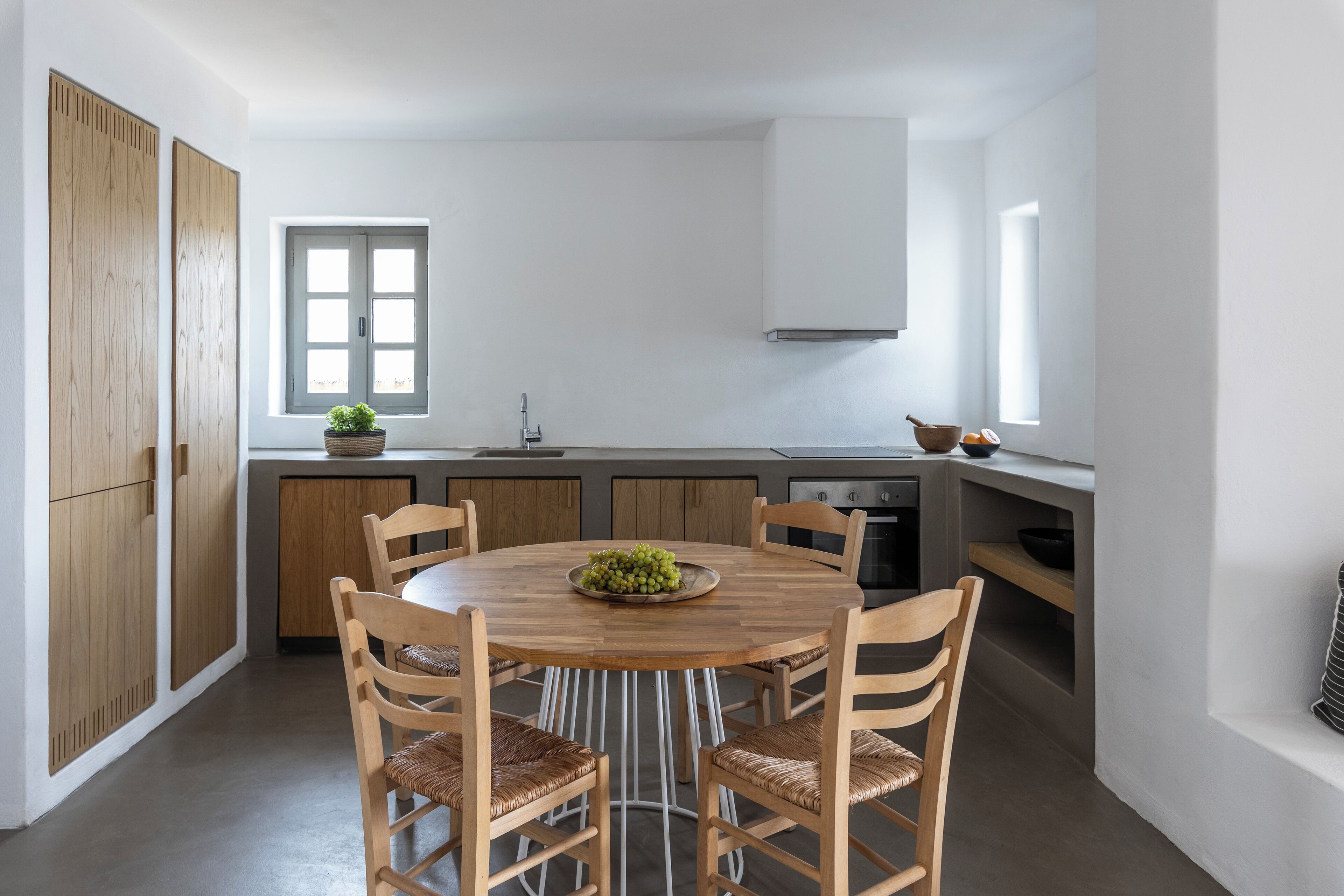 Una cocina moderna con una mesa redonda de madera, seis sillas de madera, un ventanal y un horno empotrado.