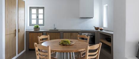 Una cocina moderna con una mesa redonda de madera, seis sillas de madera, un ventanal y un horno empotrado.