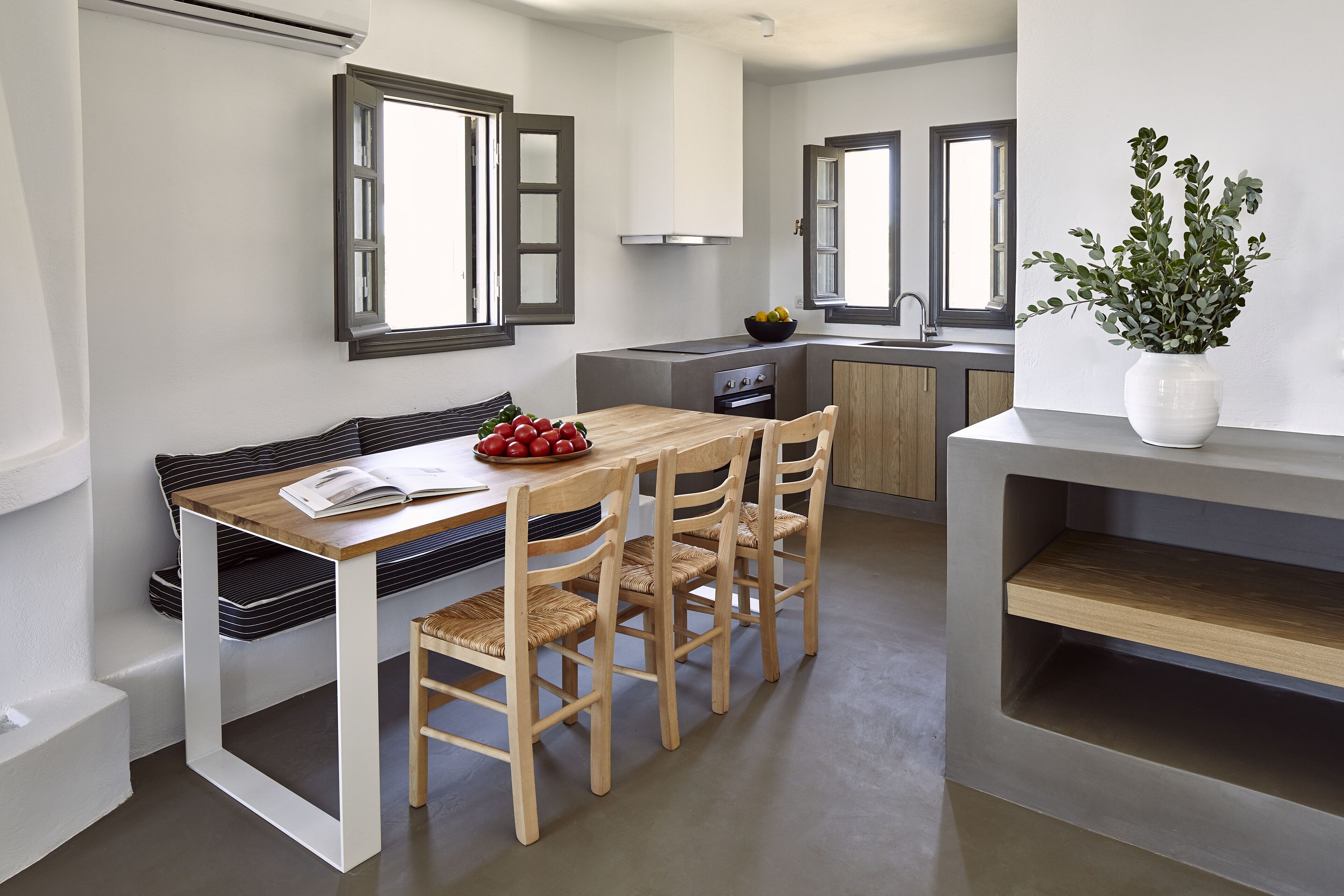 A modern kitchen with a dining area, featuring a wooden table, chairs, and a white vase with greenery.