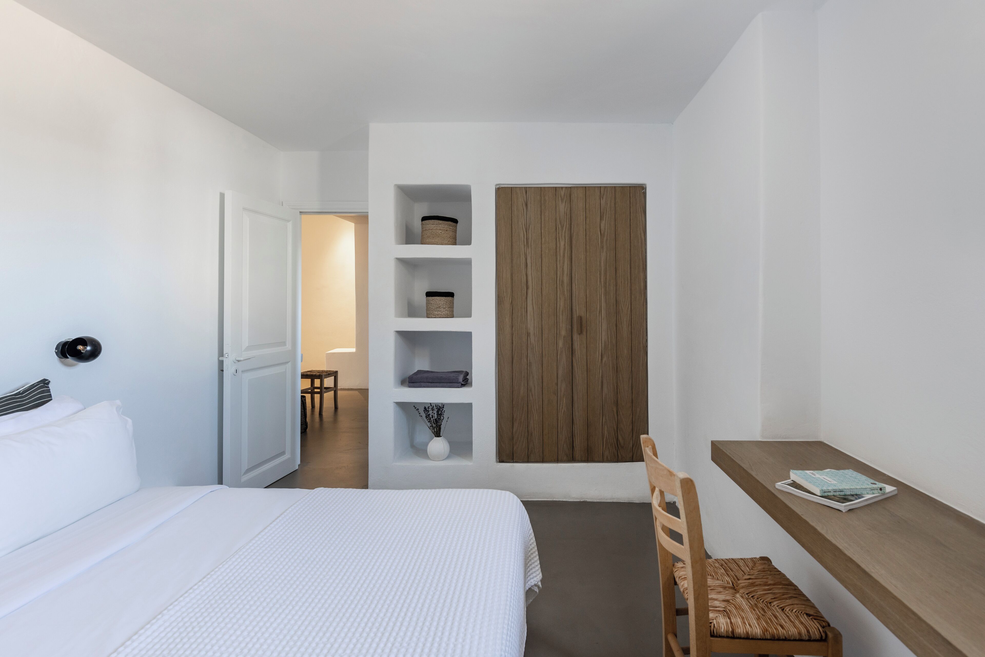 A modern hotel room with a bed, a wooden desk, and built-in shelves.