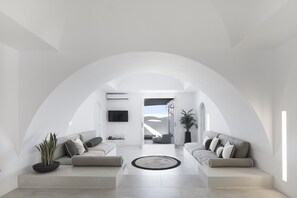 A modern, minimalist living room with a high arched ceiling, two sofas with cushions, a round rug, and a potted plant. - Le Blanc Nest (Santorini)