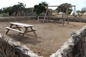 An outdoor area with a picnic table, swings, and a stone wall. - Eco Resort Bonaire (Kralendijk)