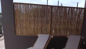 Two wooden lounge chairs with cushions on a concrete floor, a bamboo fence in the background, and a cloudy sky above. - Eco Resort Bonaire (Kralendijk)