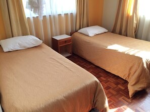 Two single beds with white pillows and beige blankets, a wooden nightstand with a small drawer, and a parquet floor.