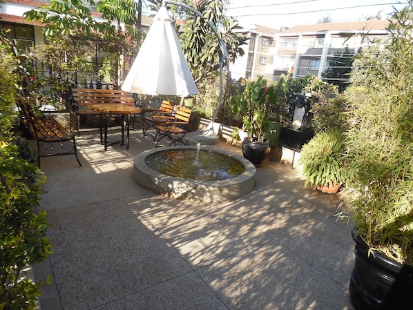 Relax in a serene outdoor space surrounded by lush greenery and a soothing fountain.