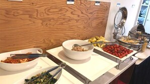 Een buffetopstelling met diverse gerechten, waaronder een kom kimchi, een bord met gesneden groenten en een schaal kersjes.