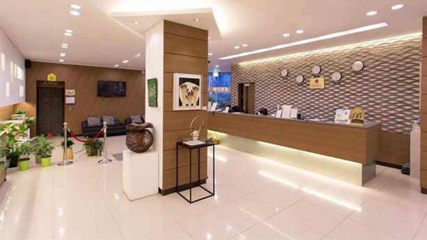 Een hotel receptie met een modern ontwerp, met een receptiebalie, een zithoek met een bank en stoelen, en een decoratieve vaas op een voetstuk.