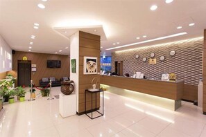Een hotel receptie met een modern ontwerp, met een receptiebalie, een zithoek met een bank en stoelen, en een decoratieve vaas op een voetstuk.