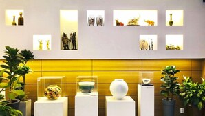 Een hotellobby met een modern design, met daaraan een reeks ingelijste kunstwerken aan de muur en plantenpotten op de vloer.