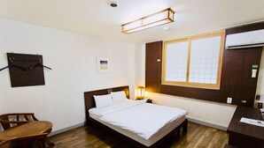 Een hotelkamer met een bed, een houten vloer, een bureau, een stoel, een raam en een luchtverkoeler aan de muur.