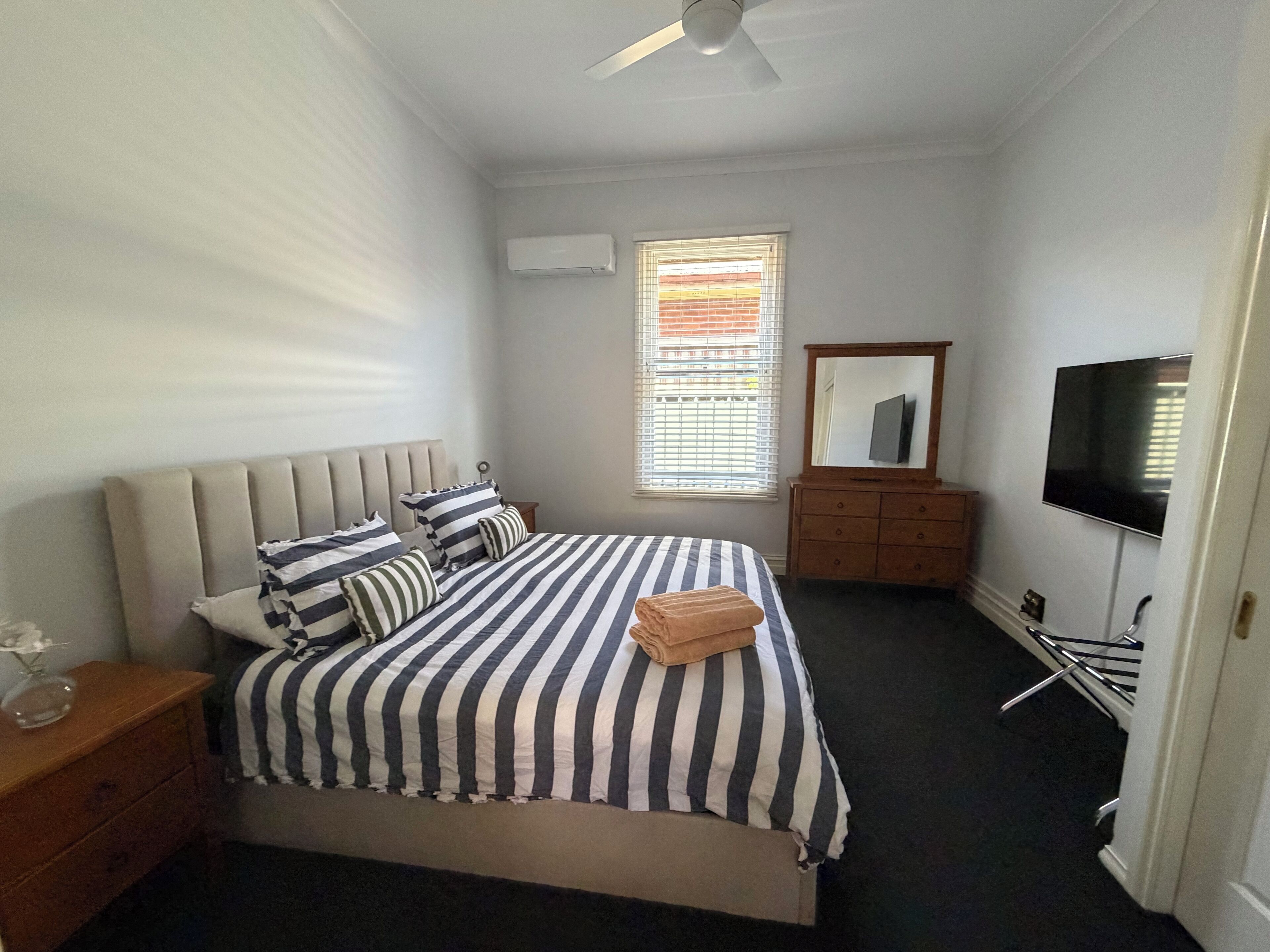 A bedroom with a bed, a dresser, a television, and a window with blinds.