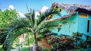 Un jardín tropical con una palmera, una mesa de madera y una edificación de techo de paja.