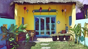 Un edificio colorido con techo de paja, una puerta azul y macetas con plantas en primer plano.