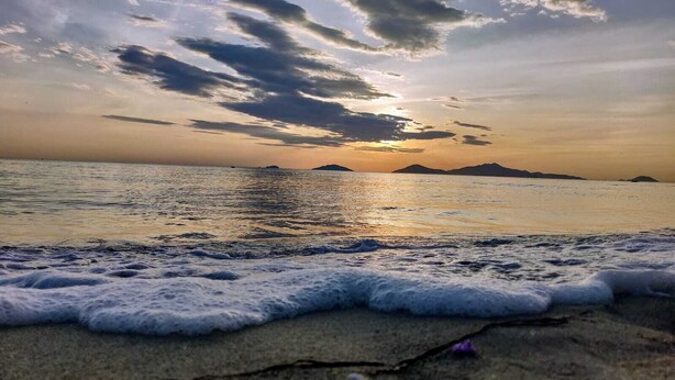 Una playa con olas al atardecer, montañas a lo lejos y un cielo despejado.