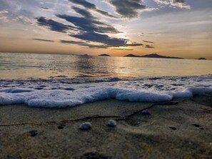 Una playa con olas al atardecer, montañas a lo lejos y un cielo despejado.