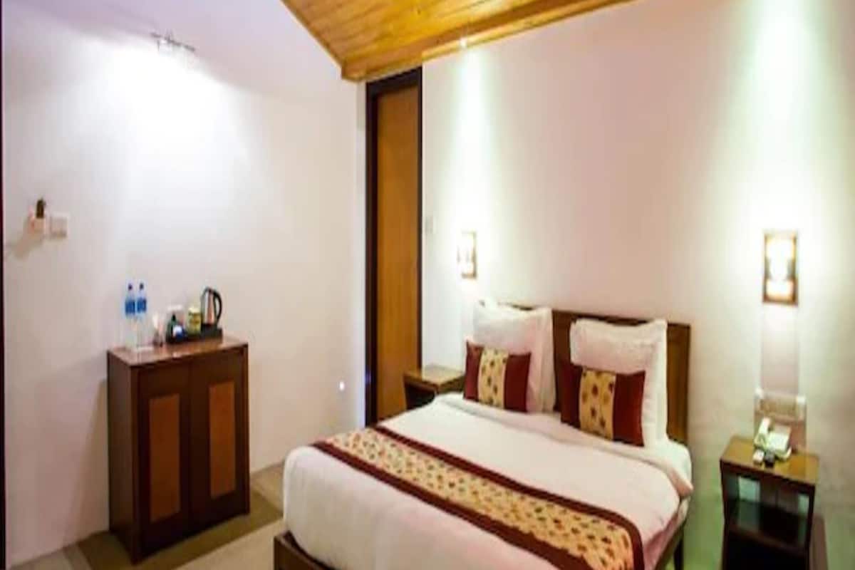 A bedroom with a wooden ceiling, a bed with a patterned bedspread, bedside tables with lamps, and a wooden dresser.