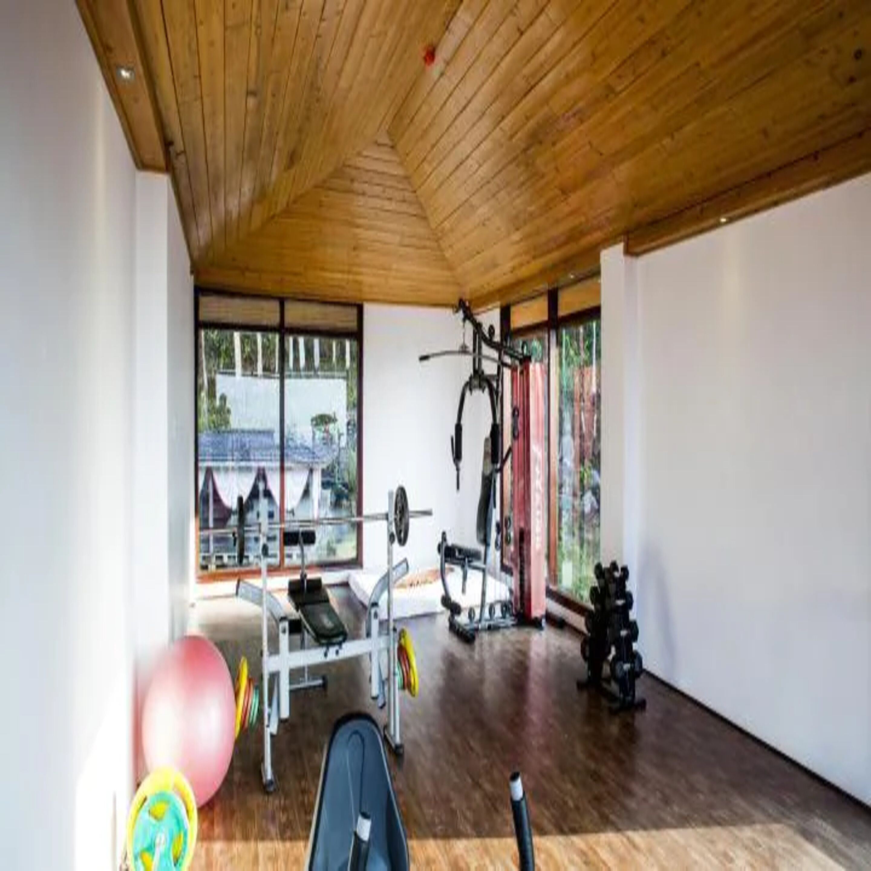 Ein Fitnessraum mit Holzboden, Trainingsgeräten und großen Fenstern.
