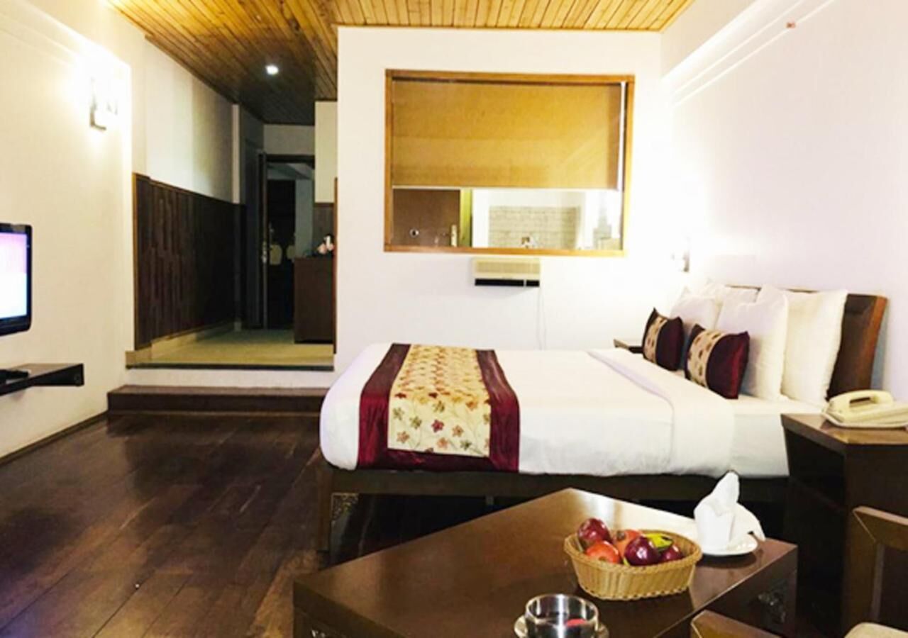 A hotel room with a bed, bedside table, and a small table with fruit.