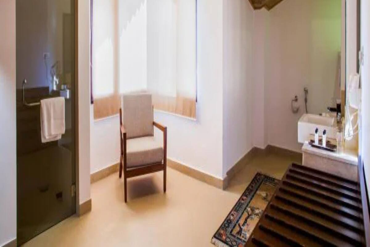 A room with a wooden ceiling, a chair, a window, a sink, and a rug.