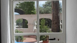 A view through a white-framed glass door to an outdoor patio with a pool, chairs, and a table. - Eremo di Montevergine : Calipso, cozy apartment with panoramic view (Forio)