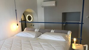 A hotel room with a bed, a bedside table with a lamp, an air conditioning unit, and a circular mirror on the wall. - Eremo di Montevergine : Calipso, cozy apartment with panoramic view (Forio)