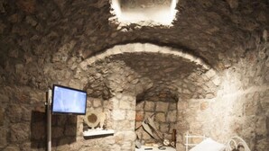 A stone-walled room with a bed, a television, and a tiled floor.