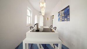A dining area with a white table, four chairs, a coffee pot, and a wall-mounted painting.