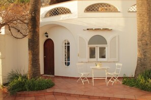 A white building with a wooden door, arched windows, and a small patio with a table and chairs. - Eremo di Montevergine : Teti, romantic and panoramic, ideal for couples (Forio)