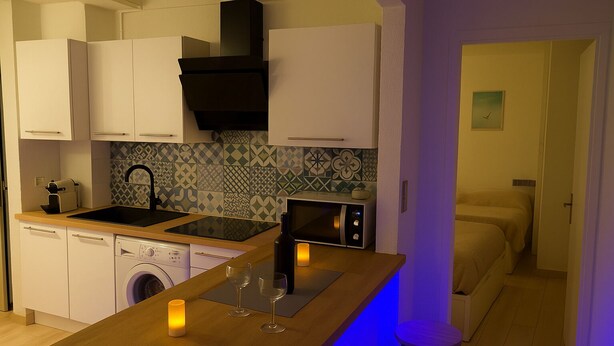 A compact kitchen with a washing machine, a microwave, and a sink. There is a bar area with stools and a small table. - Exceptional Sea View – Sunrise Guaranteed! (Canet-en-Roussillon)