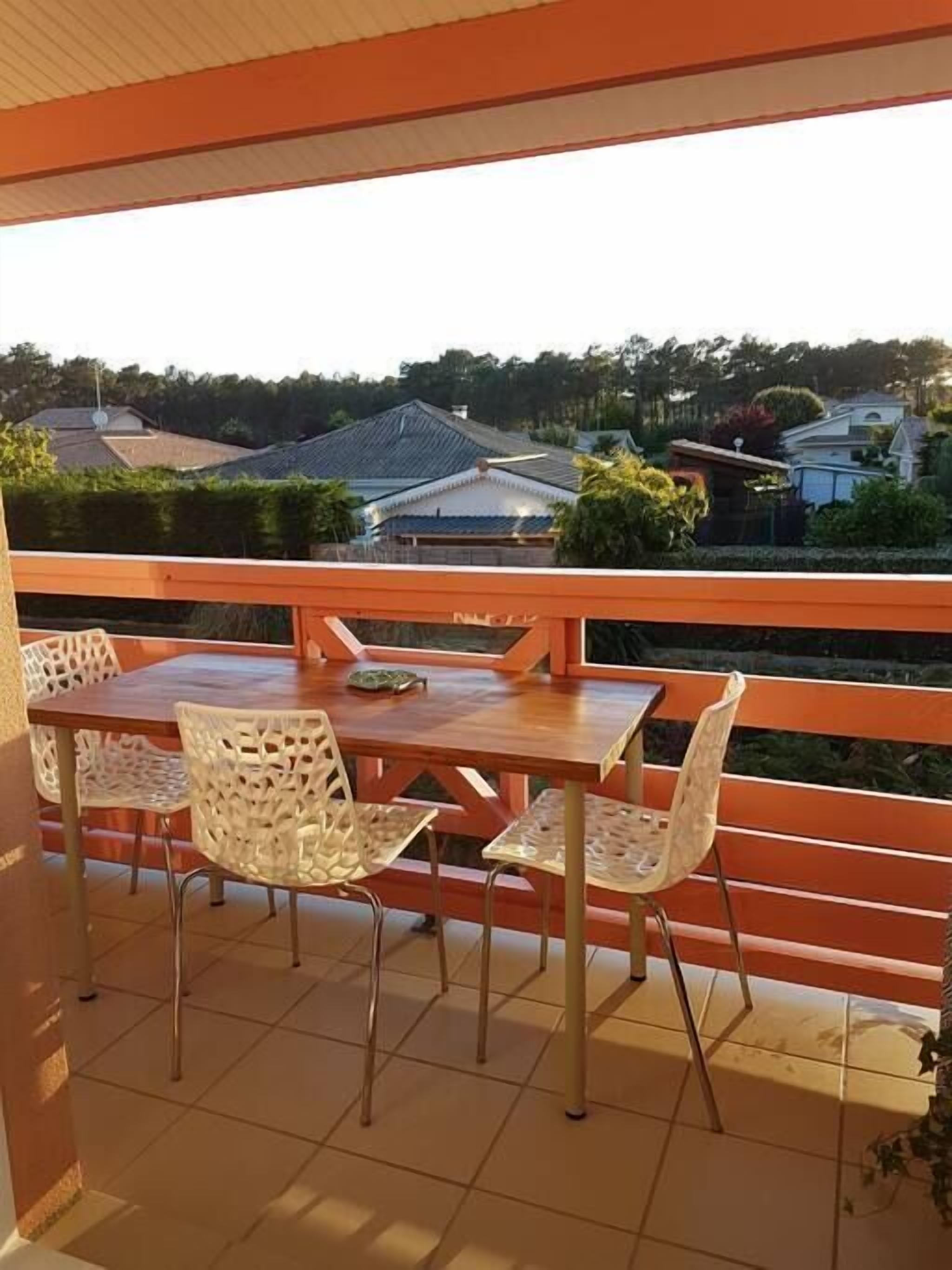 A balcony with a wooden table and four chairs, overlooking a residential area with houses and greenery.