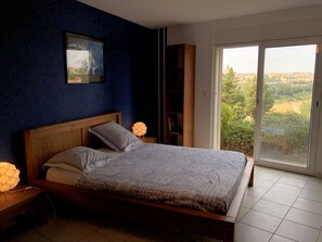 Relax in this serene retreat with a large bed, nightstand, and bookshelf, offering a peaceful view of the surrounding greenery.