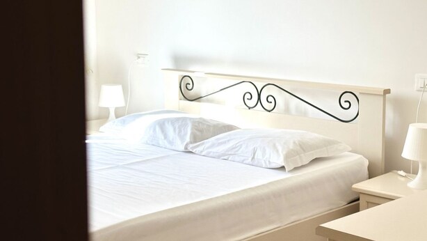 Ein ordentlich bezogenes Bett mit weißen Laken, einem schlichten Kopfteil und Nachttischlampen.