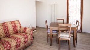 Ein Wohnzimmer mit einer Couch, einem Esstisch mit Stühlen, einem Heizkörper und einer Tür mit Vorhängen.