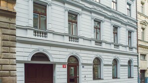 Um edifício branco com uma porta marrom grande, várias janelas e uma pequena varanda.