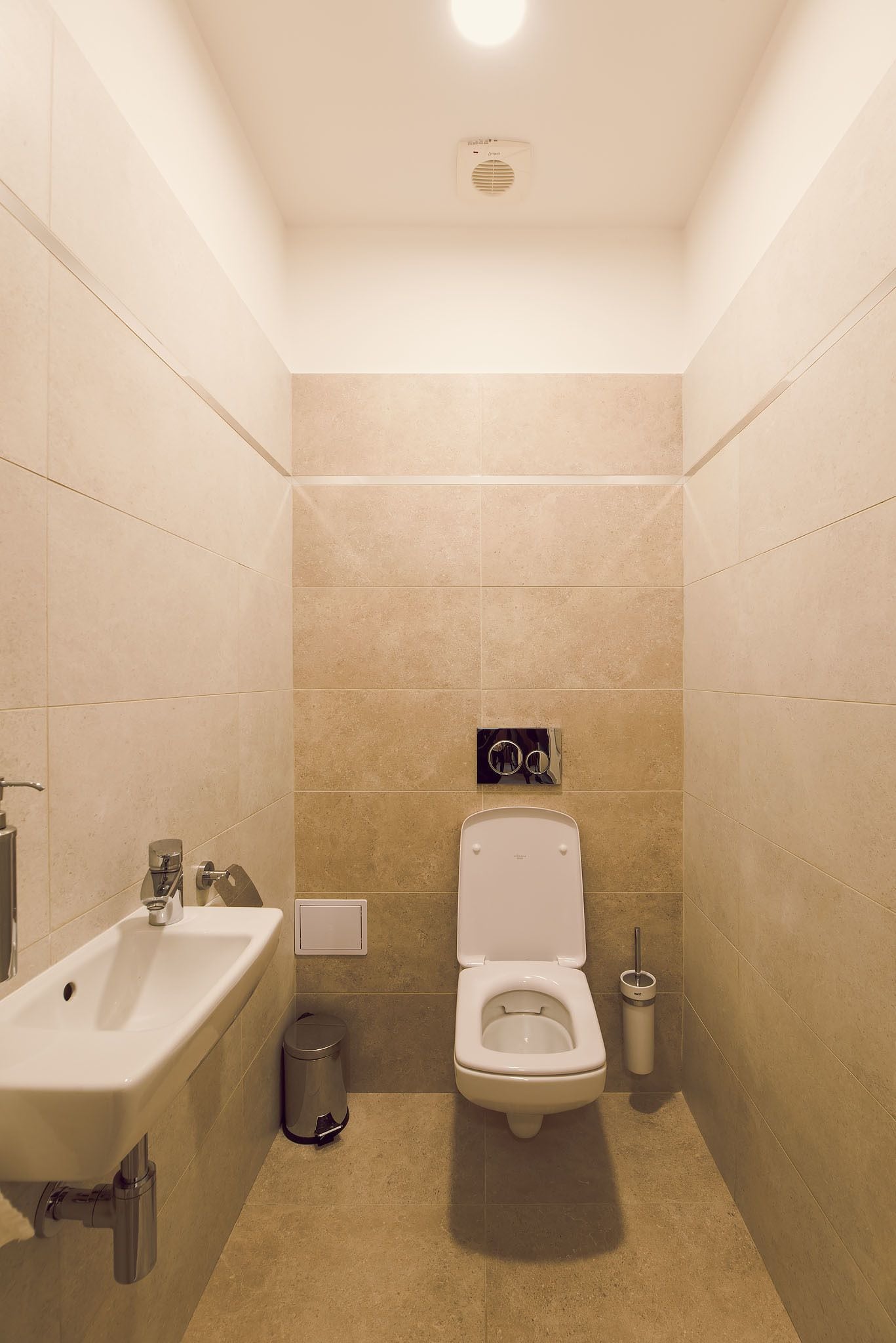 A small, modern bathroom with a toilet, bidet, sink, and trash can.